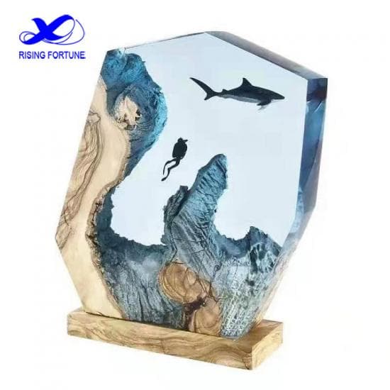 En dekorativ harpiksskulptur av Rising Fortune, som viser en undervannsscene med en dykker og en hai. Stykket har en klar blå Glassklar Epoxy - CCR Epoxy Entropy SuperSap-seksjon som representerer vann, lik et elvebord, treaksenter som ligner undervannsterreng, og en naturlig trebase. Rising Fortune-logoen er øverst i venstre hjørne.